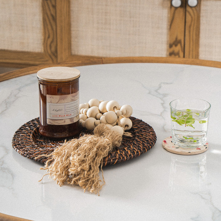 A-glass-of-water-and-a-candle-placed-on-a-dark-brown-woven-charger-on-a-white-marble-table