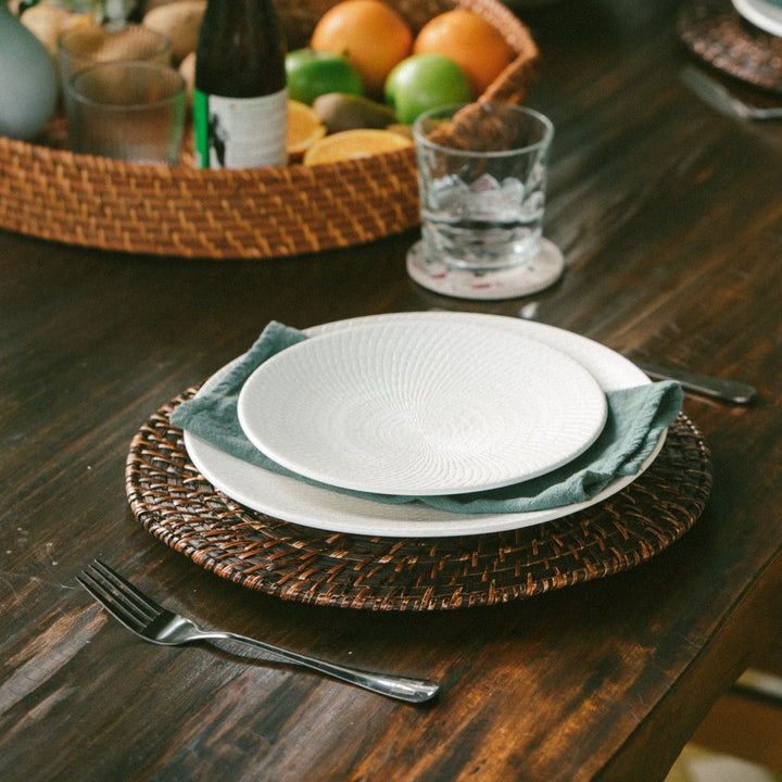 a-white-plate-with-a-smaller-white-bowl-on-top-set-on-a-dark-brown-woven-charger-with-a-green-napkin