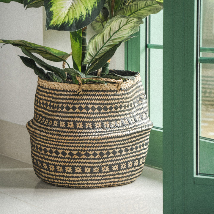 A-black-patterned-seagrass-large-planter-vase-holding-a-plant-placed-near-a-open-door