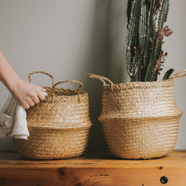 Two neutral shade seagrass wicker planter vases, one with a plant and one with a towel