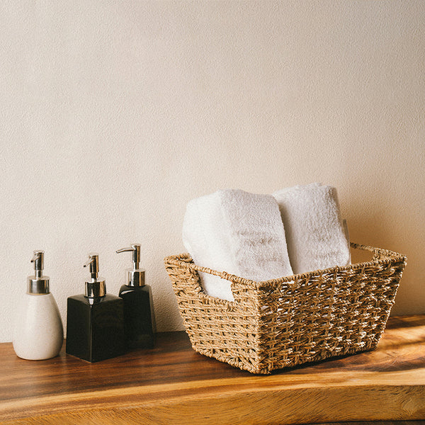 A twisted seagrass wicker storage basket filled with bathroom towels on a wooden table