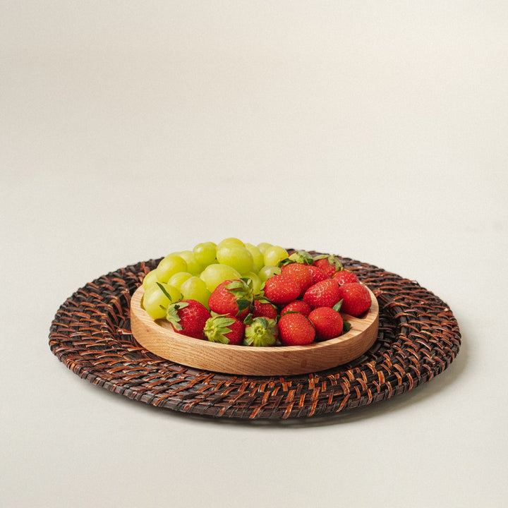 a-wooden-bowl-filled-with-green-grapes-and-red-strawberries-placed-on-a-dark-brown-woven-charger