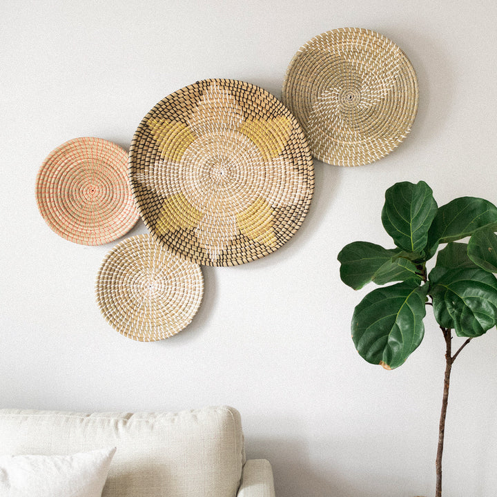 A living room with a brown leather sofa, a large cactus, and four wall decor baskets, displayed on a white wall