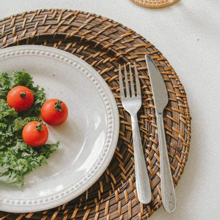 A-white-plate-with-a-few-tomatoes-and-lettuce-placed-on-a-brown-woven-charger