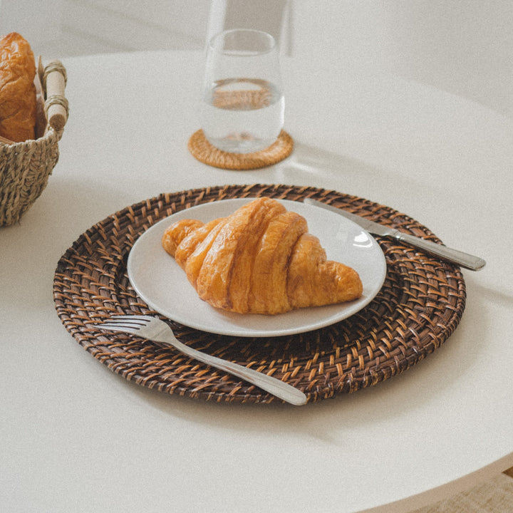 A-croissant-on-a-white-plate-placed-on-a-dark-brown-woven-charger