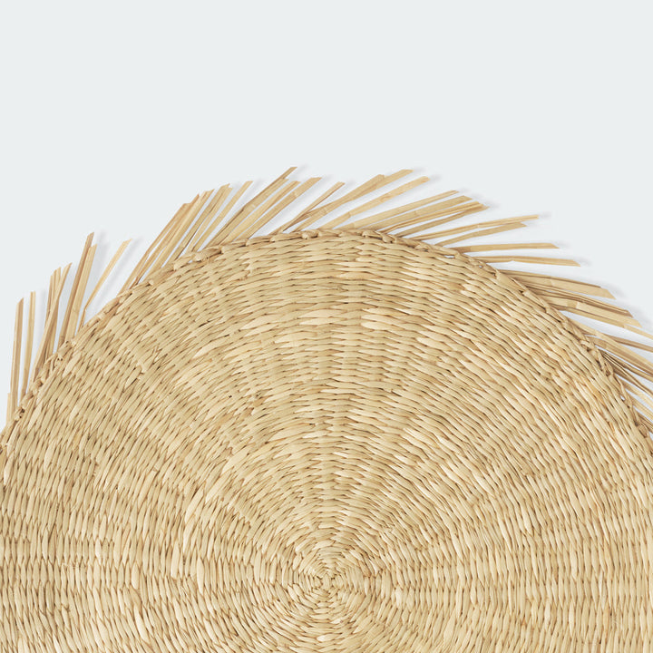 A half-slide look at a round seagrass woven placemat with a white plate above