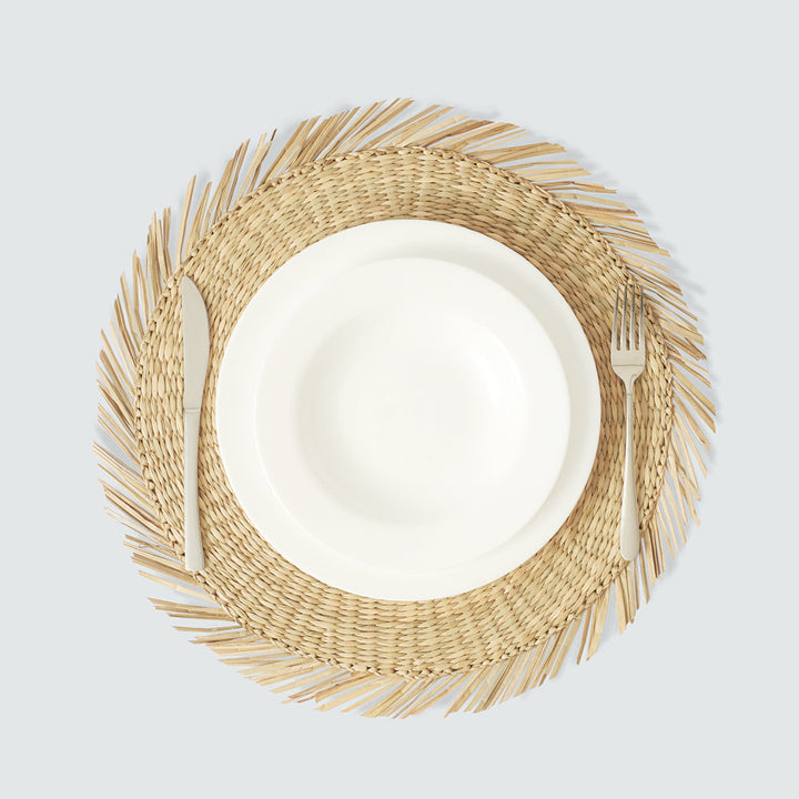 A round woven seagrass placemat with a white plate of pear on the table