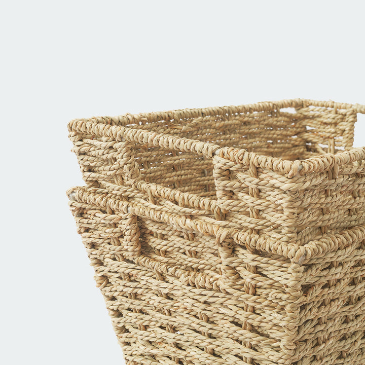 A close-up above the corner of a seagrass wicker basket with built-in handles